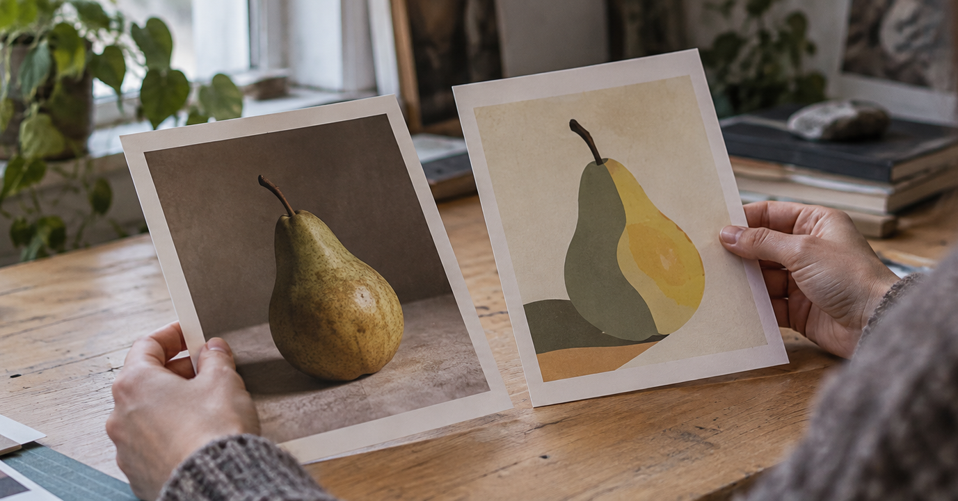 A person holds two prints side by side, a photograph of a pear and an illustration of the same fruit, above a wooden table.